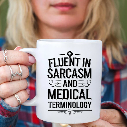 White ceramic coffee mug with bold black text that says 'Fluent in Sarcasm and Medical Terminology', held by a woman in a plaid shirt—perfect gift for nurses, medical workers, and healthcare professionals with a sense of humor. Funny nurse mug for coworkers, medical school grads, or sarcastic doctors and EMTs