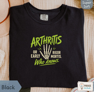 	Black funny aging shirt with a skeleton hand and green and white lettering reading “Arthritis or early rigor mortis. Who knows.”
